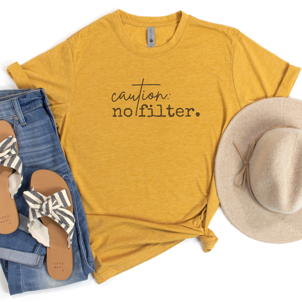 Yellow t-shirt with 'caution: no filter.' text, paired with denim jeans, sandals, and a hat on a white background.
