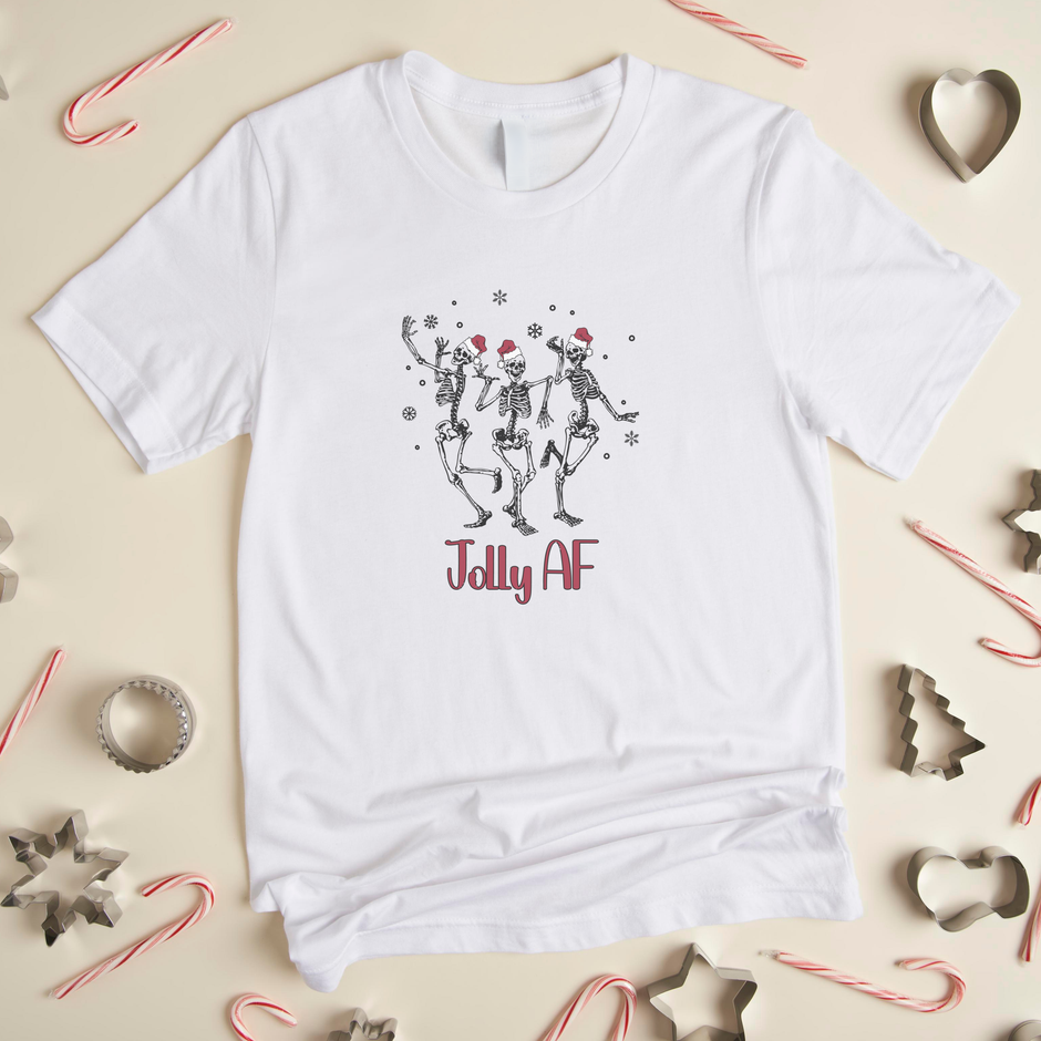 White t-shirt with dancing skeletons design and 'Jolly AF' text on a festive background with candy canes and cookie cutters.