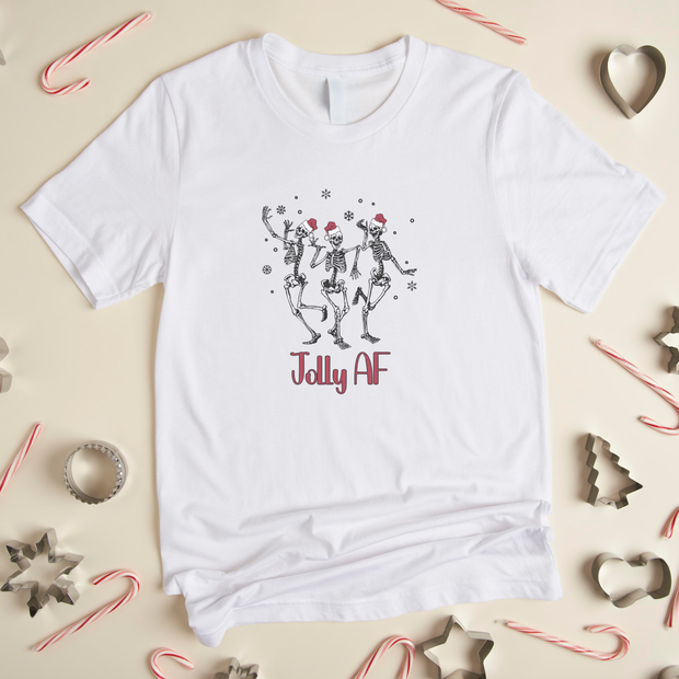 White t-shirt with dancing skeletons design and 'Jolly AF' text on a festive background with candy canes and cookie cutters.