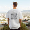 Person wearing a white t-shirt with a QR code on the back, standing against an urban landscape.