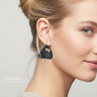 Close-up of a woman wearing a black clip-on earring with a design on a plain background