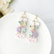 A pair of floral patterned earrings featuring an Easter bunny design, with clip-on closures, displayed on a white plate.