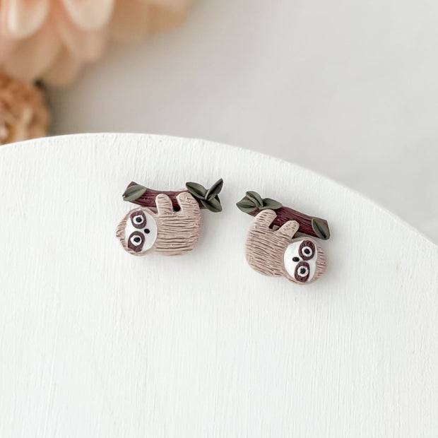 Sloth-shaped earrings on a white surface with a blurred background