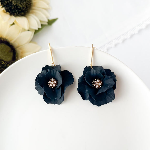 Black flower earrings with gold centers on a white plate with sunflowers in the background