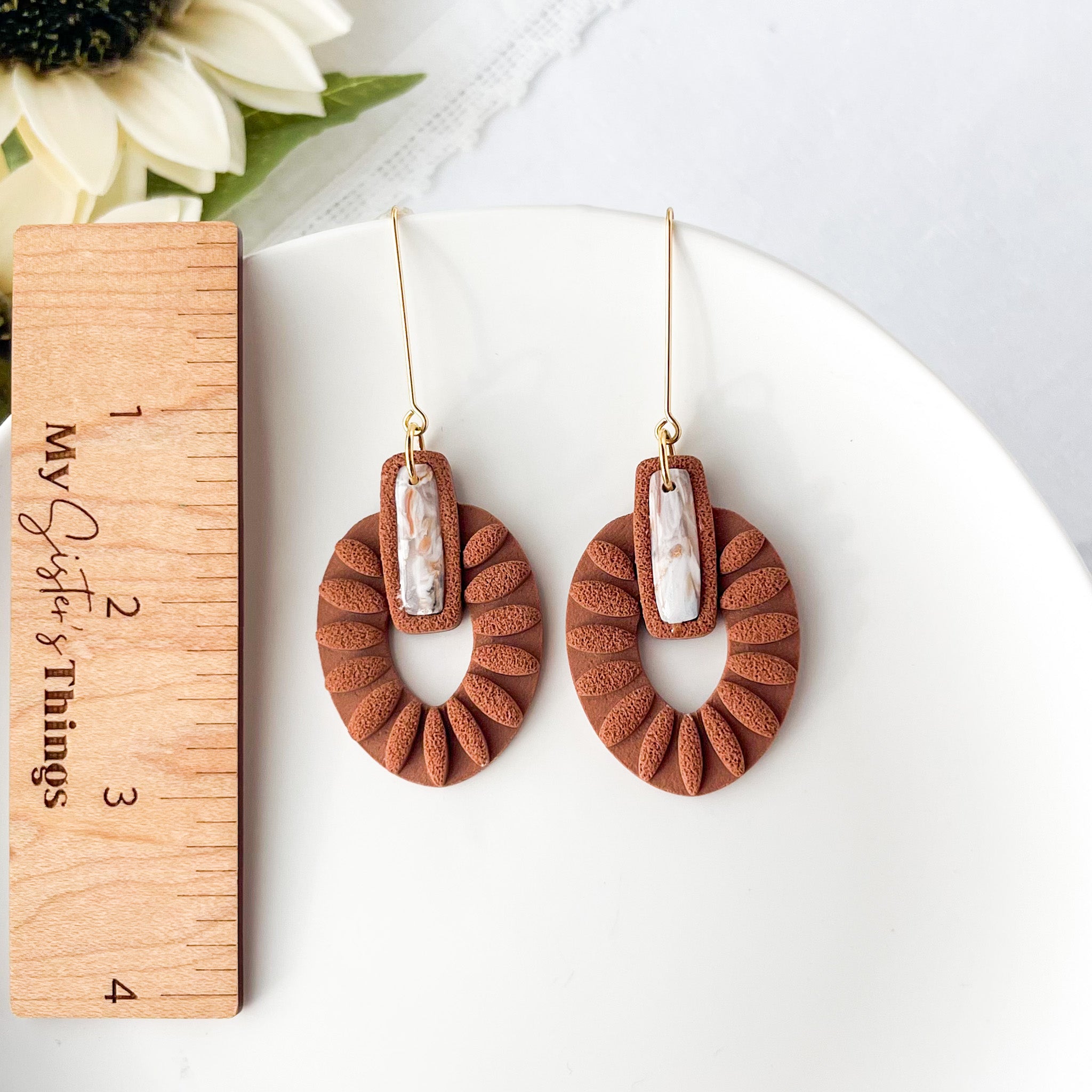 Brown textured earrings with a central stone, displayed on a white surface with a wooden ruler for scale.