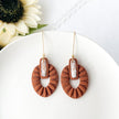 Brown textured earrings with white stones on a white plate with flowers in the background