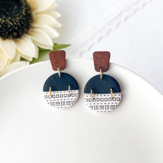 Pair of earrings with wooden tops and black and white printed polymer clay  on a white surface with sunflower in the background