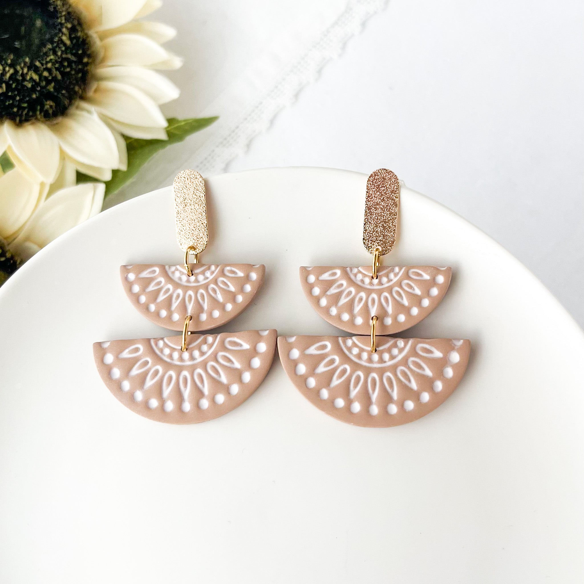 Pair of earrings with half-circle design on a white plate with flowers in the background