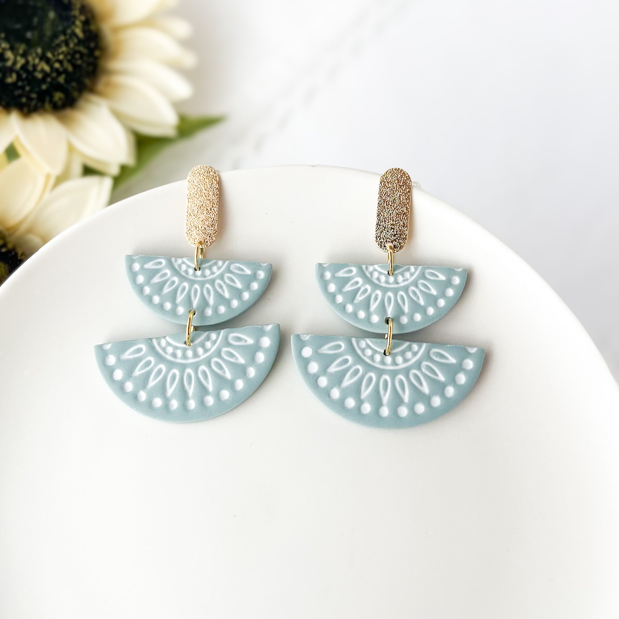 Pair of blue geometric earrings on a white plate with flowers in the background