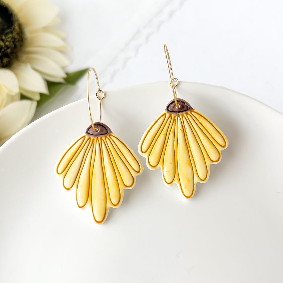 Yellow flower-shaped earrings on a white plate with a blurred background