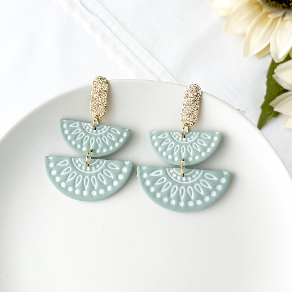 Pair of light green earrings with decorative patterns on a white surface.