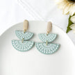 Pair of light green earrings with decorative patterns on a white surface.