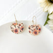 Floral patterned earrings on a white surface with flowers in the background