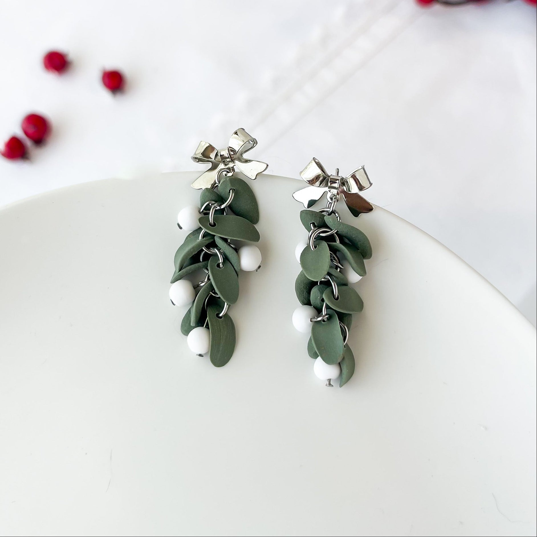 Pair of green leaf-like earrings with white beads on a white surface.