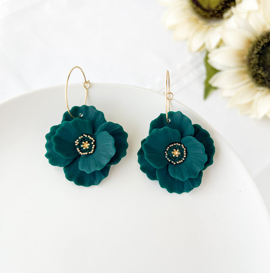Dark forrest green flower earrings on a white plate with sunflowers in the background