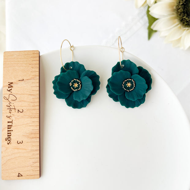 Teal flower earrings with gold centers on a white surface next to a wooden ruler.