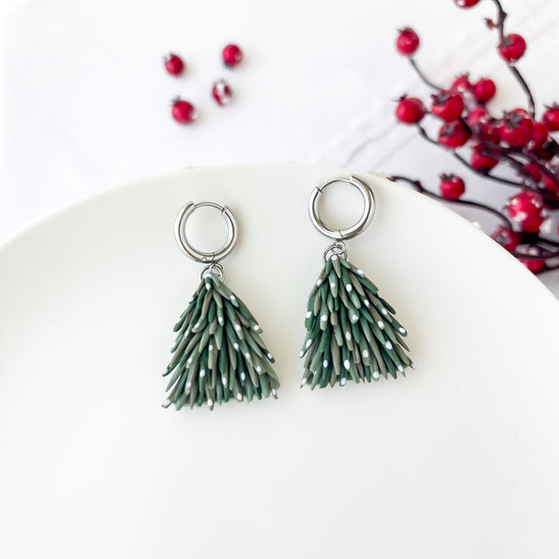 Green christmas tree earrings on a white plate with red berries in the background