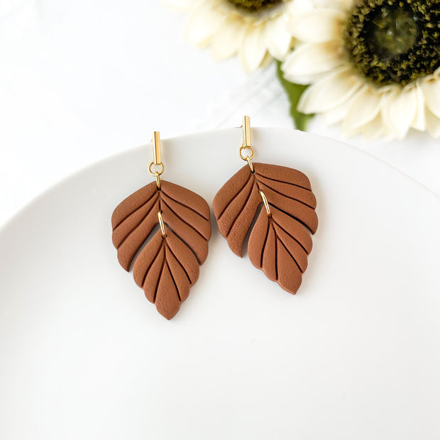 Brown leaf-shaped earrings on a white plate with flowers in the background