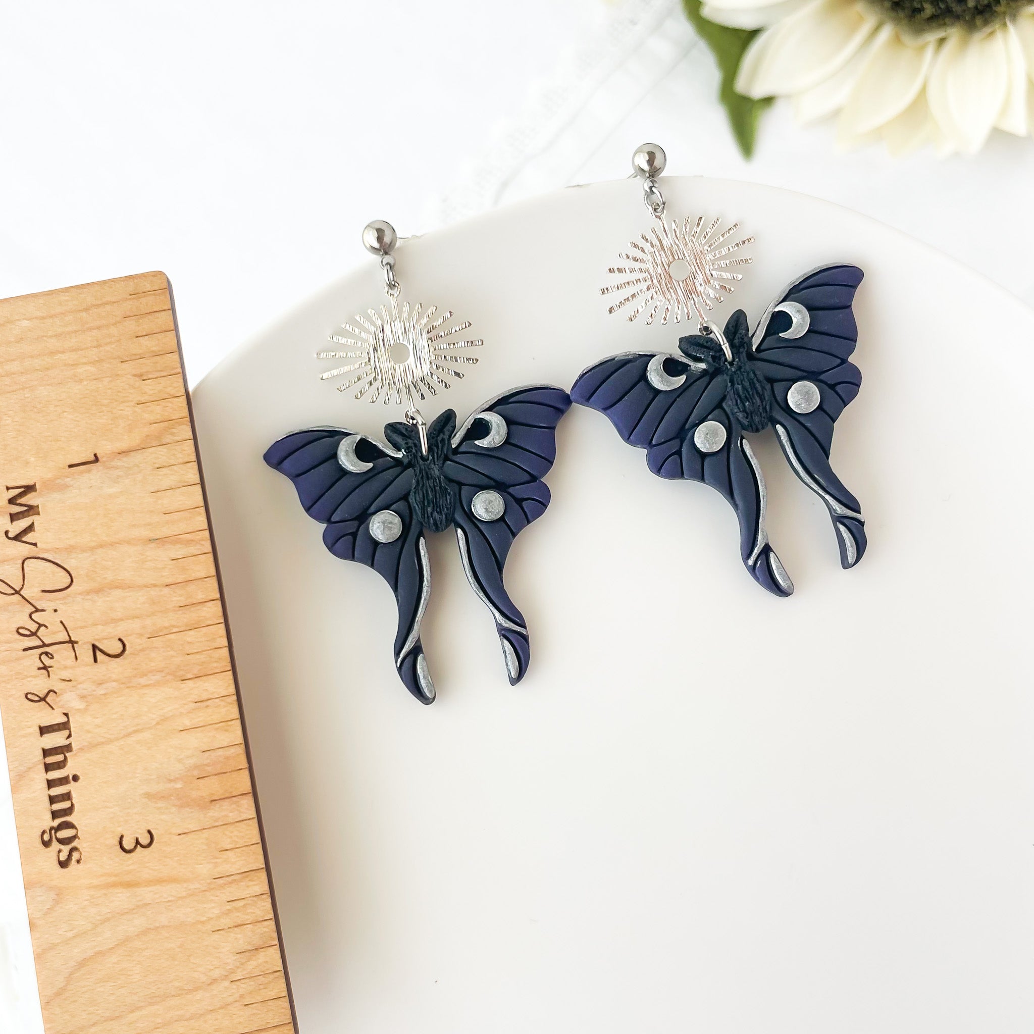 Moth-shaped earrings on a white surface with a wooden ruler for scale.