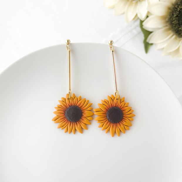 Sunflower-shaped earrings on a white plate with flowers in the background