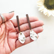 Hand holding two earrings with a blurred sunflower in the background