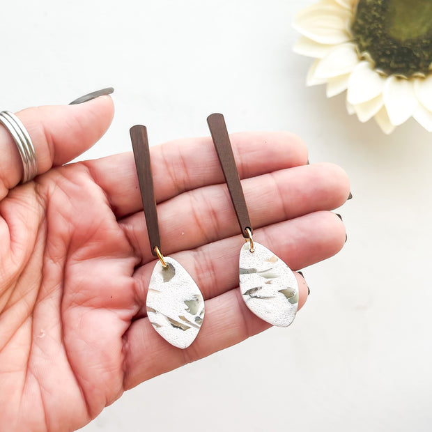 Hand holding two earrings with a blurred sunflower in the background