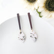 Marble-patterned earrings with brown sticks on a white surface with sunflowers in the background