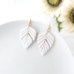 White leaf-shaped earrings on a white surface with sunflowers in the background