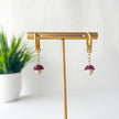 Gold hoop earrings with red and white mushrooms on a gold stand against a white background with a plant.