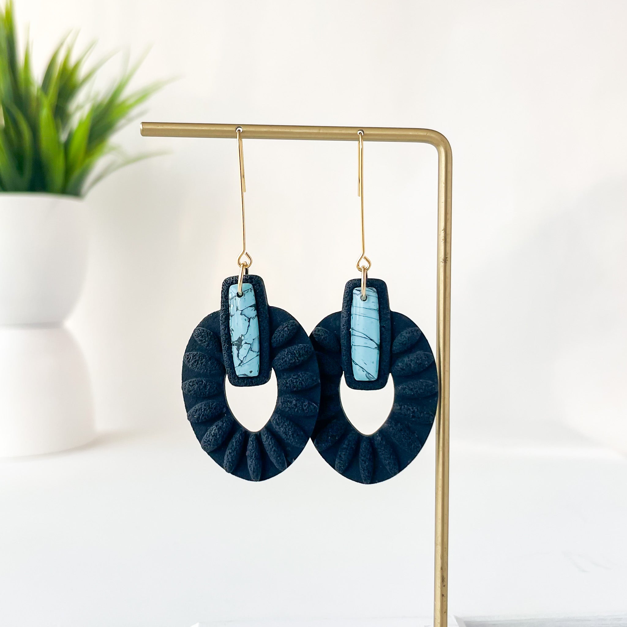Blue and black earrings on a gold stand with a white background