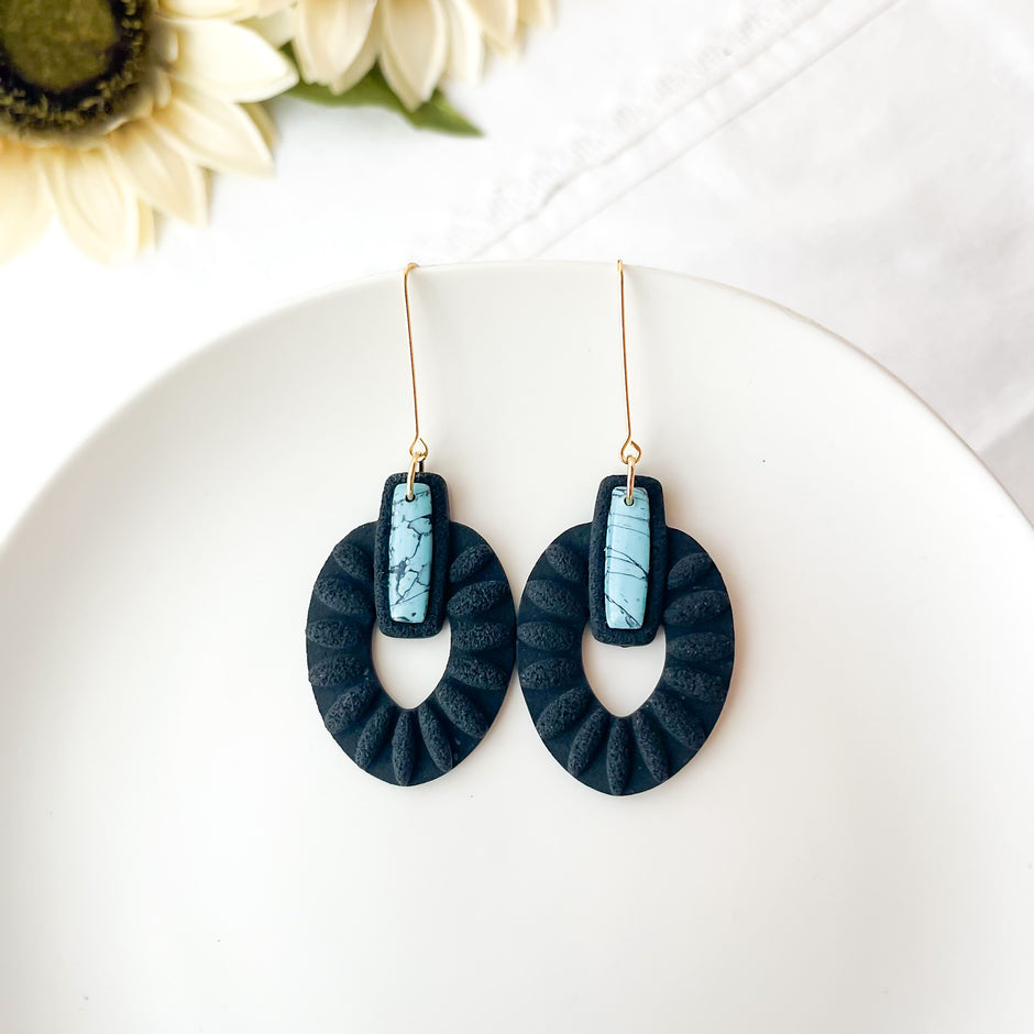 Blue earrings with turquoise stones on a white plate with flowers in the background
