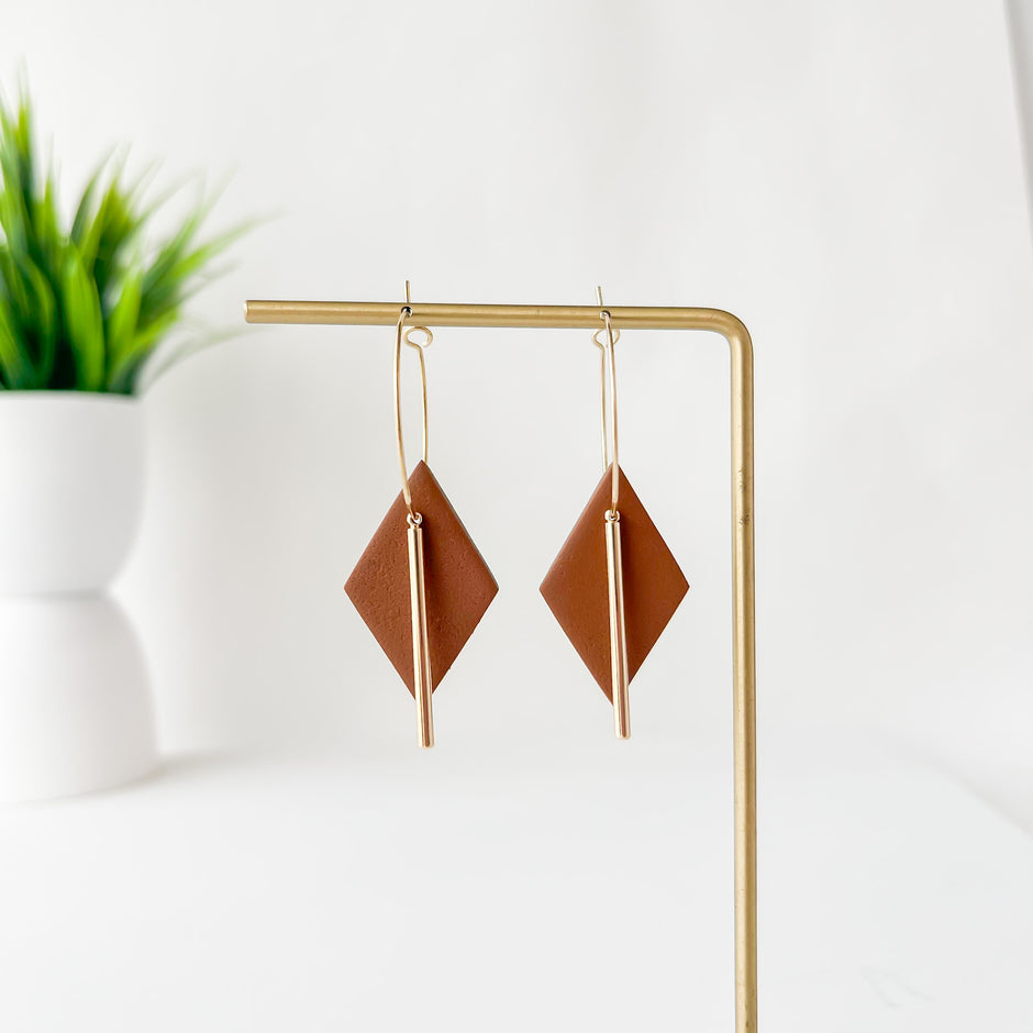 Pair of geometric earrings on a gold stand with a plant in the background