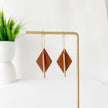 Pair of geometric earrings on a gold stand with a plant in the background