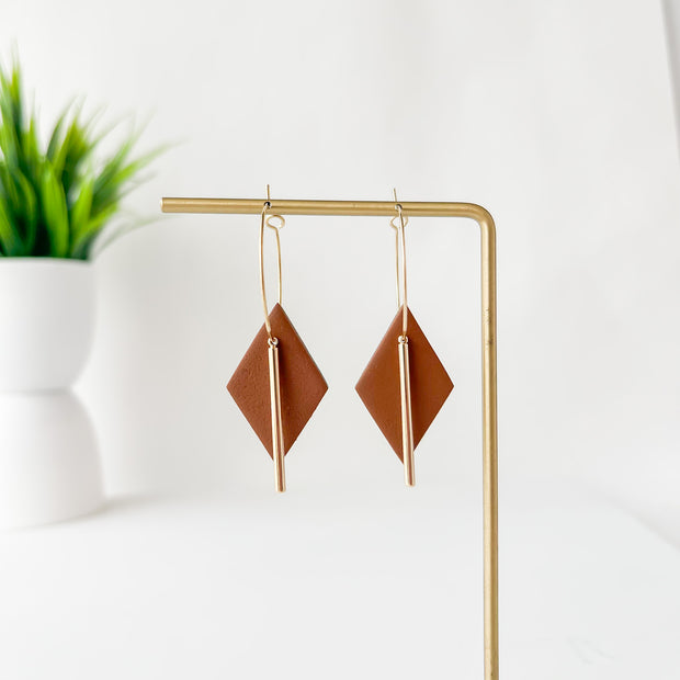 Pair of geometric earrings on a gold stand with a plant in the background