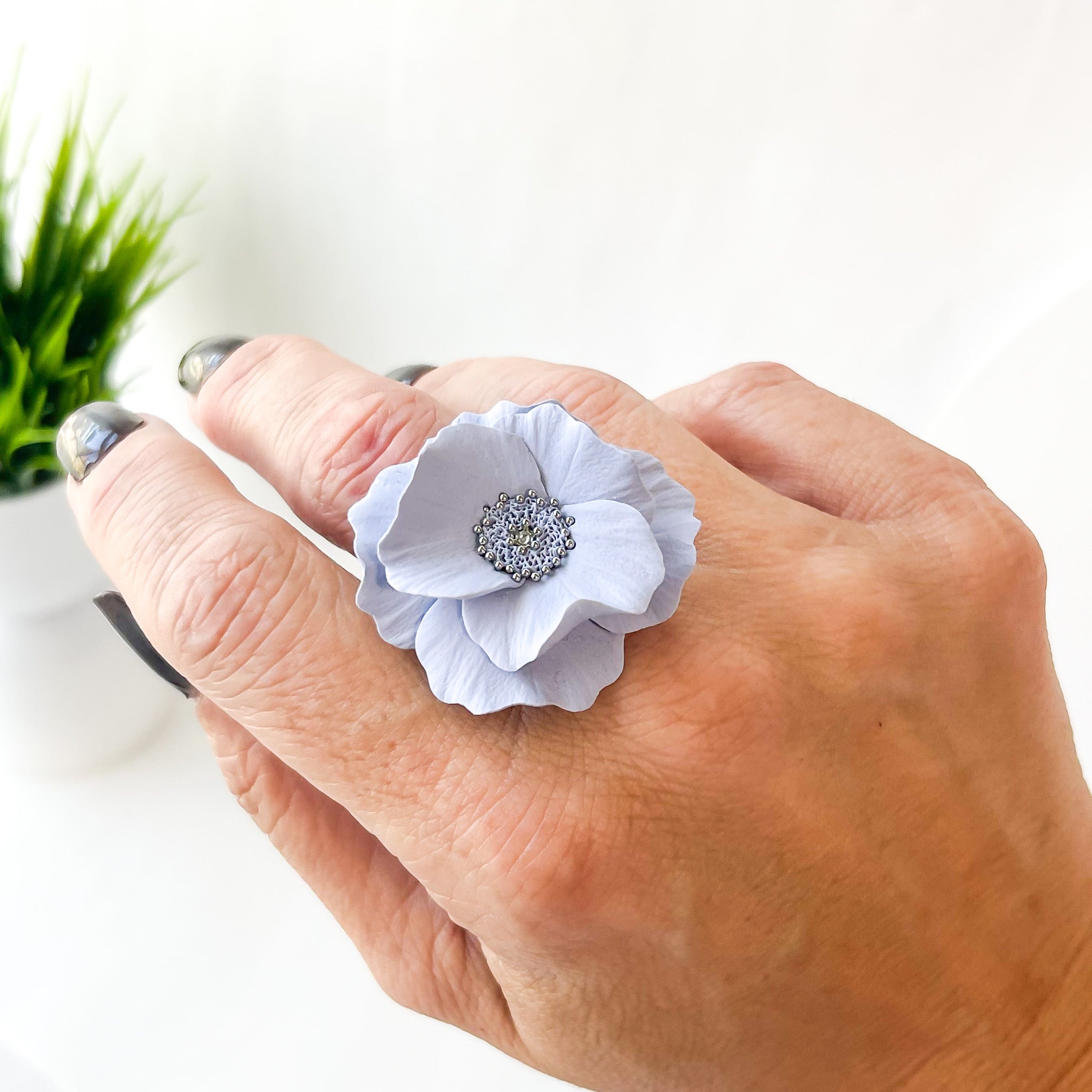 Hand wearing a white floral ring with a silver center on a blurred background