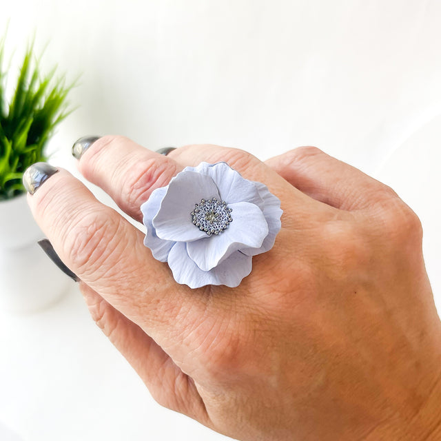 Hand wearing a white floral ring with a silver center on a blurred background