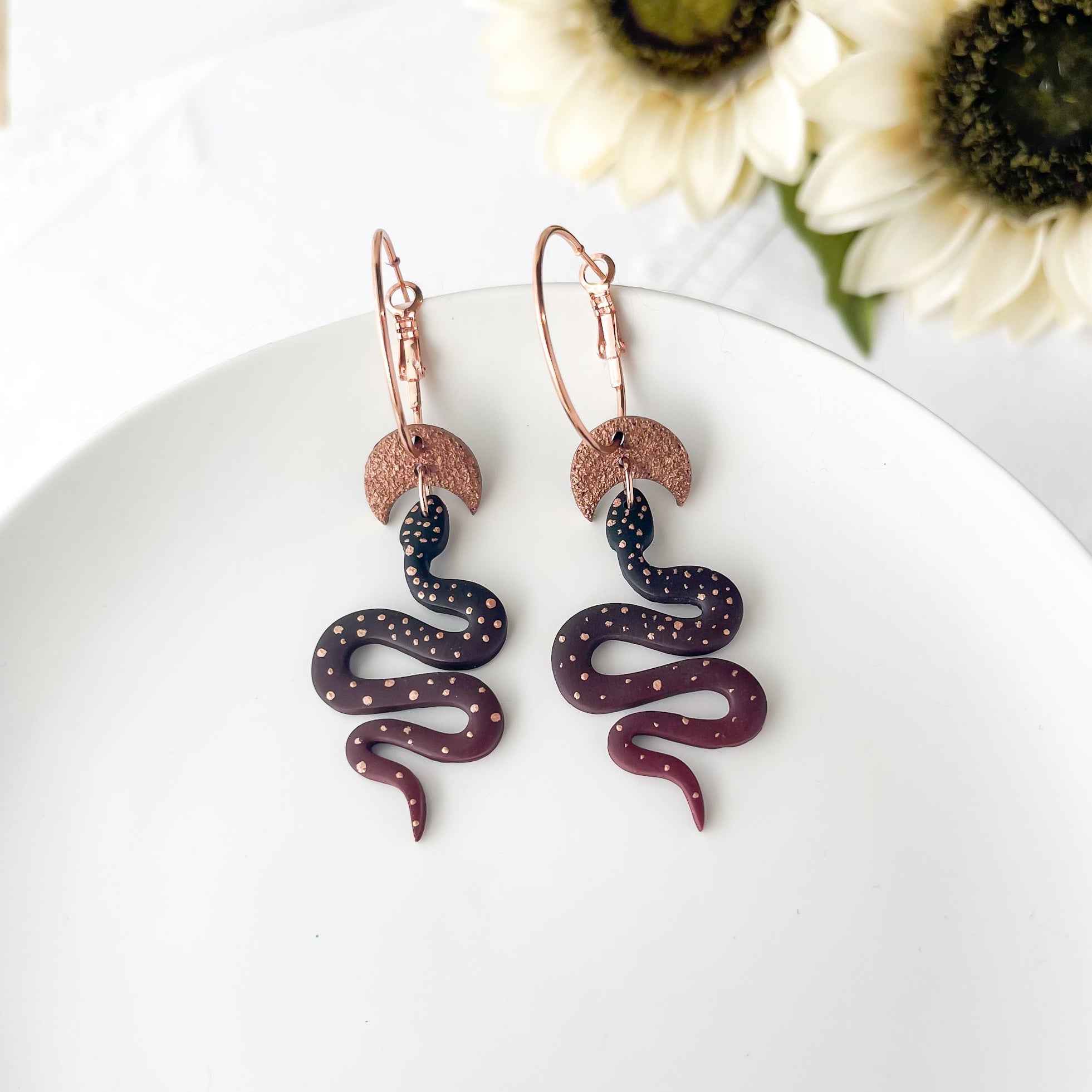 Snake-shaped earrings on a white plate with flowers in the background