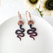 Snake-shaped earrings on a white plate with flowers in the background