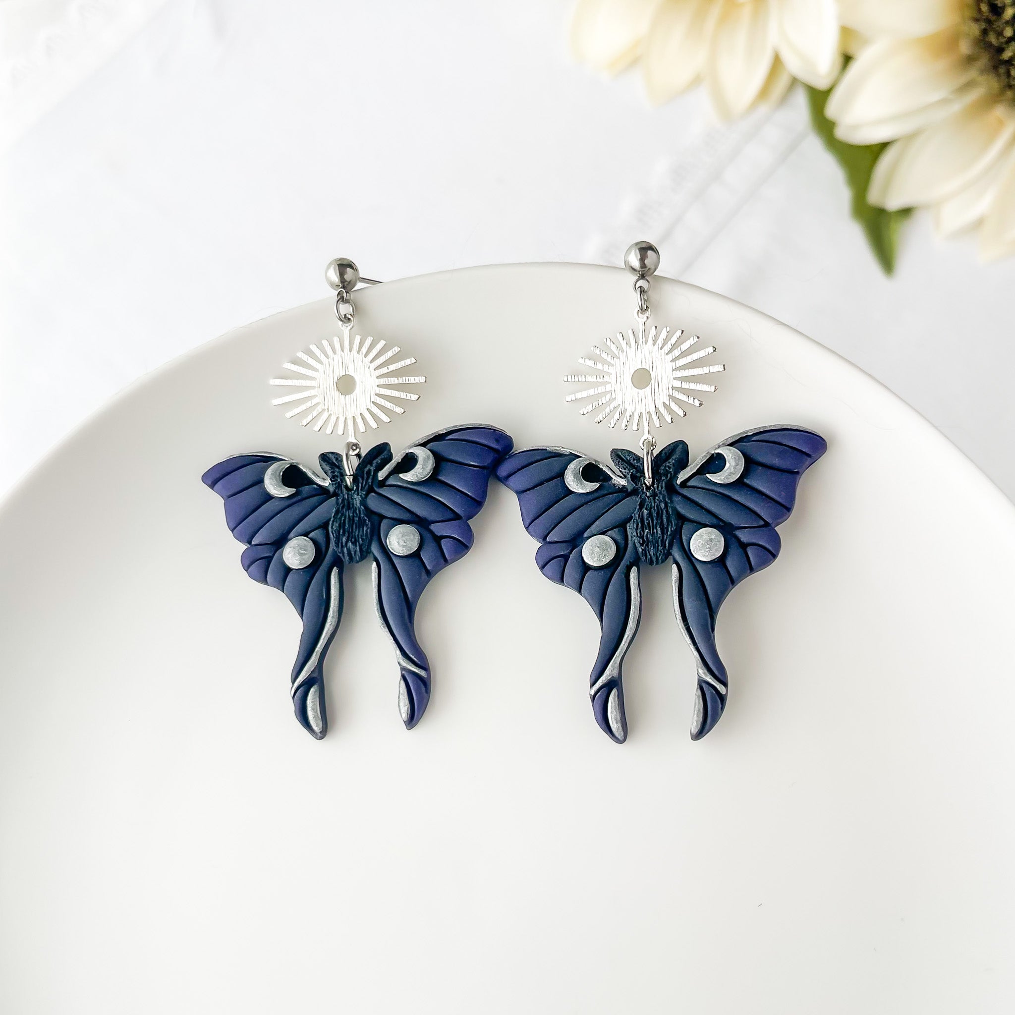 Moth-shaped earrings on a white plate with flowers in the background