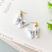 Butterfly-shaped earrings with floral details on a book page background