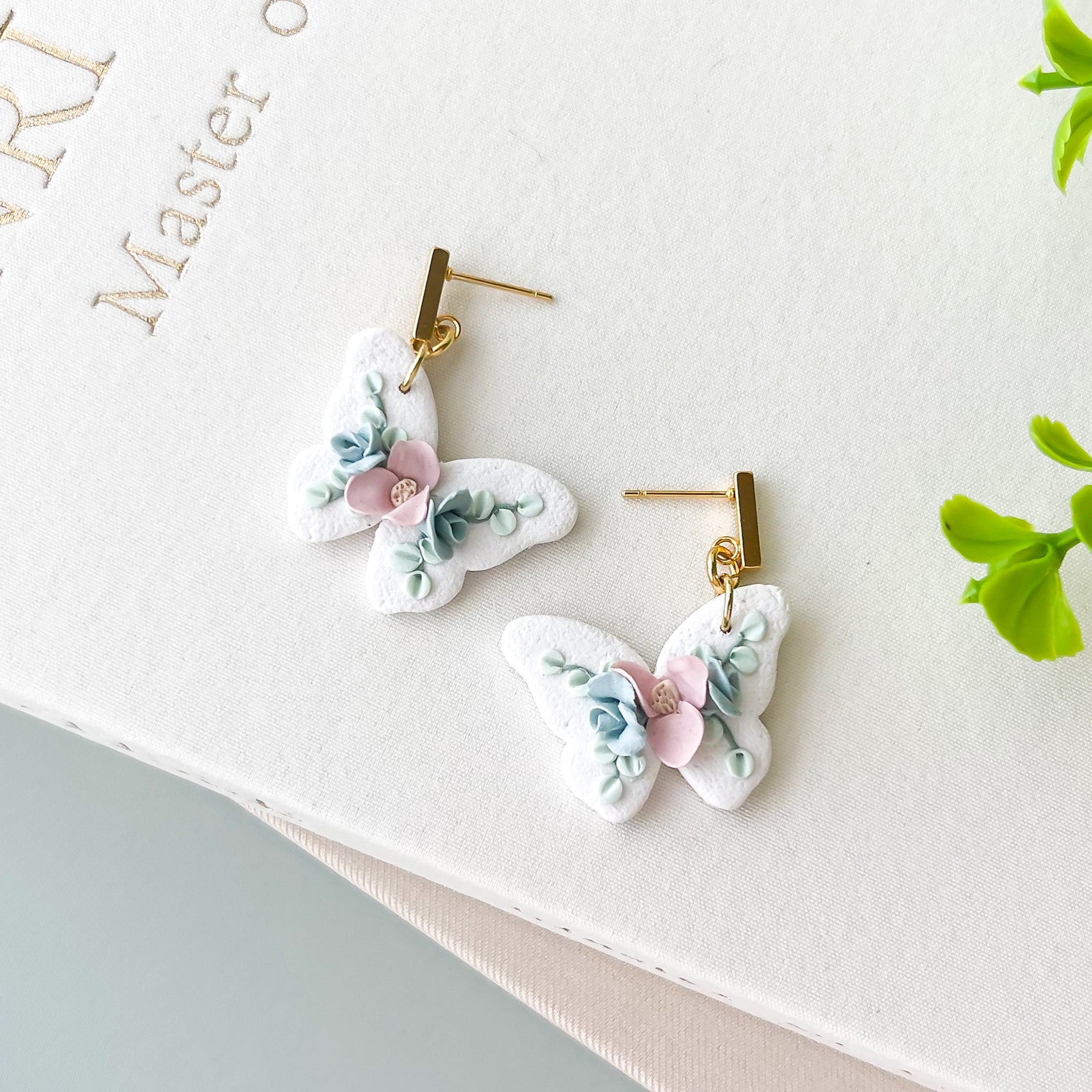 Butterfly-shaped earrings with floral details on a white surface.