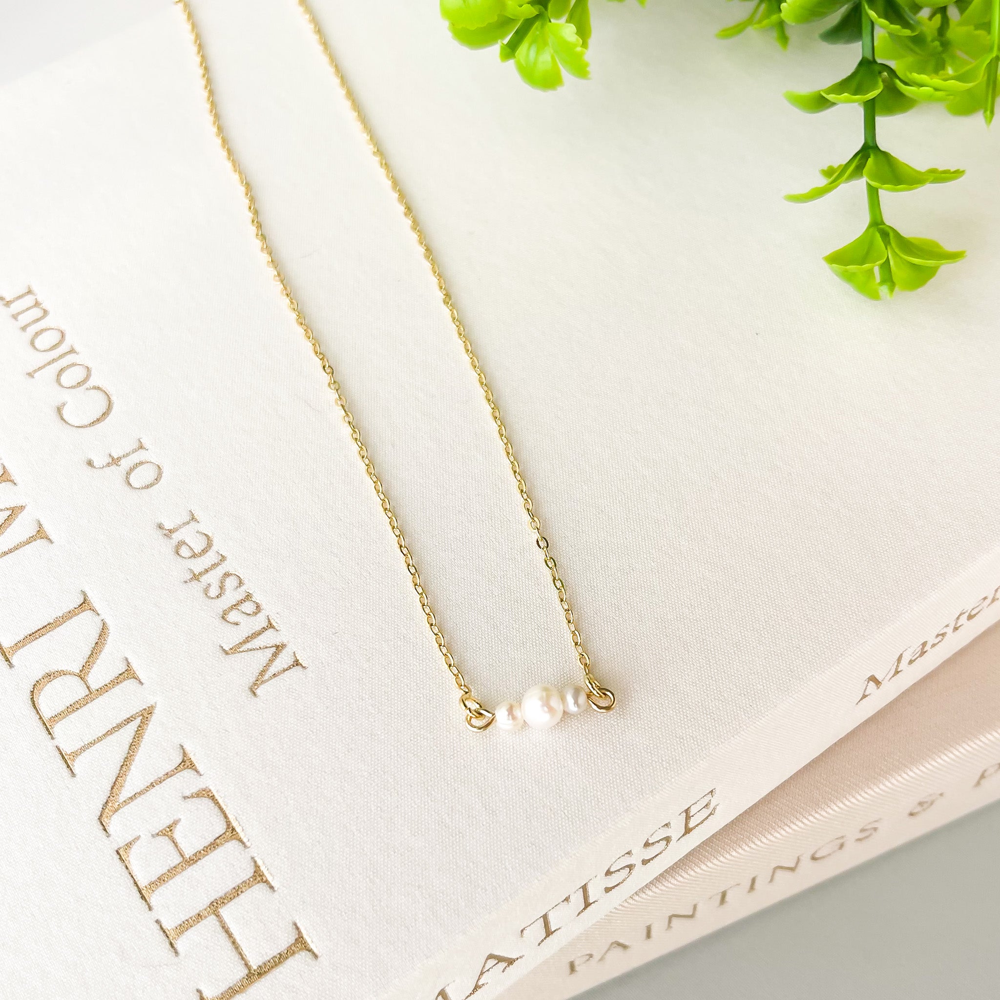 Gold necklace with a pearl pendant on a book with greenery in the background