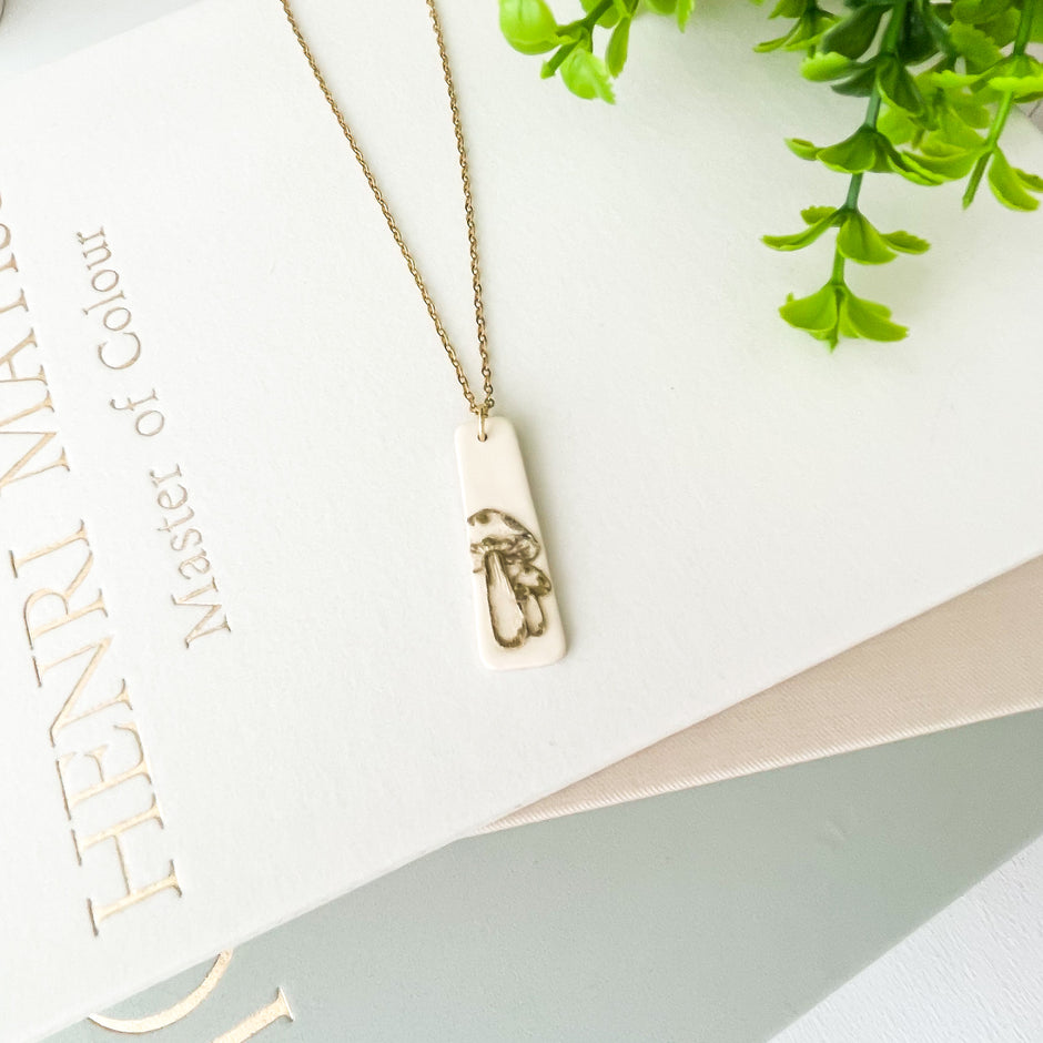 Necklace with a mushroom design pendant on a white surface with text and greenery