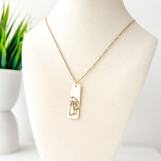 Gold necklace with a rectangular mushroom design pendant on a mannequin bust.