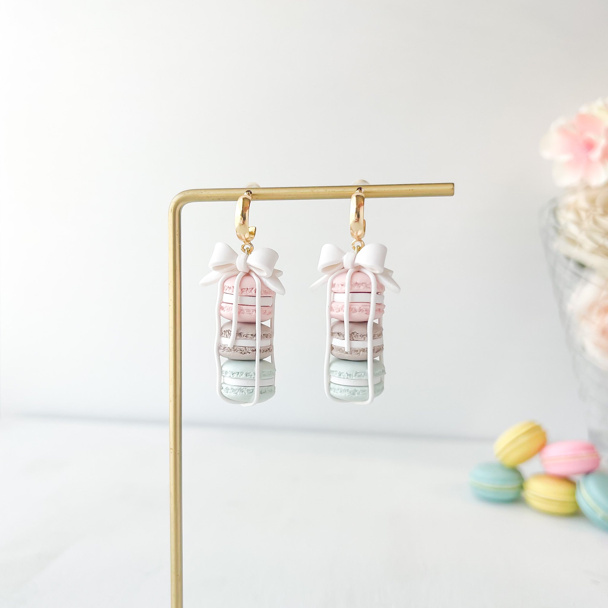 Pair of macaron earrings with a bow on a stand with pastel macaron decorations on a light background