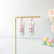 Pair of macaron earrings with a bow on a stand with pastel macaron decorations on a light background