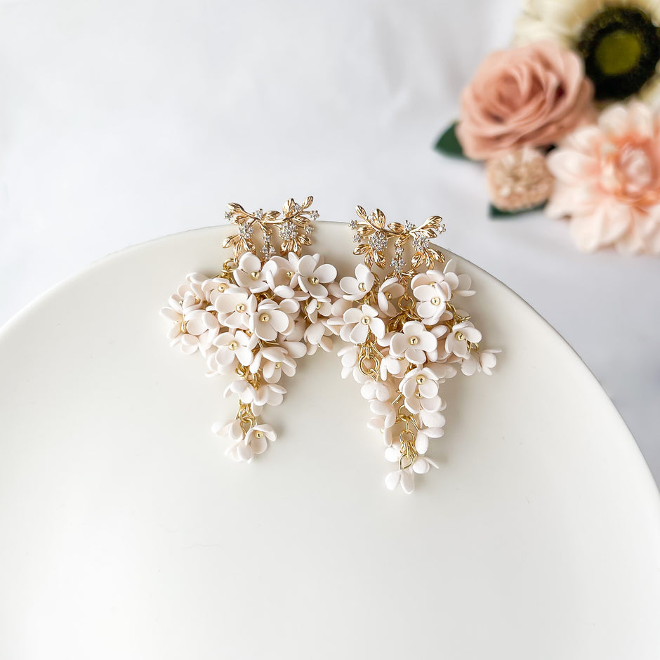 Decorative white floral earrings on a white surface with flowers in the background