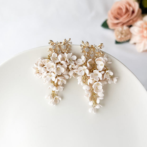 Decorative floral earrings on a white surface with flowers in the background
