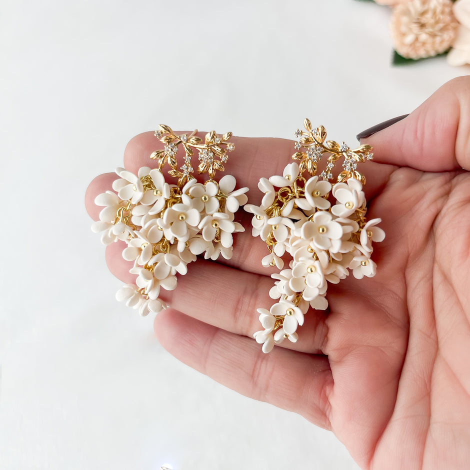 Hand holding a pair of floral earrings with gold accents on a light background