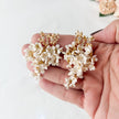 Hand holding a pair of floral earrings with gold accents on a light background